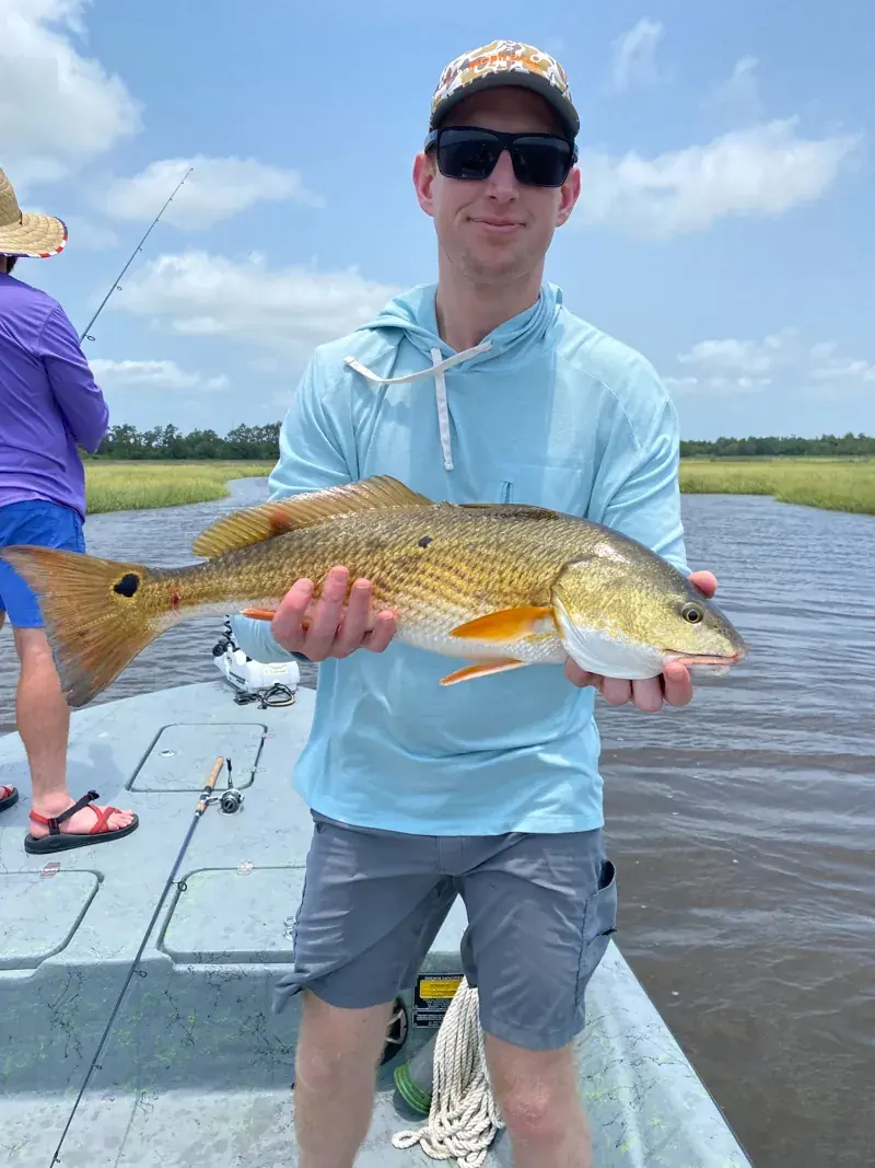 Client holding a redfish horizontally with marsh grass behind the boat