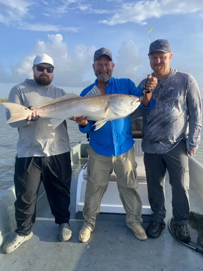 Three anglers holding a large redfish together aboard the boat