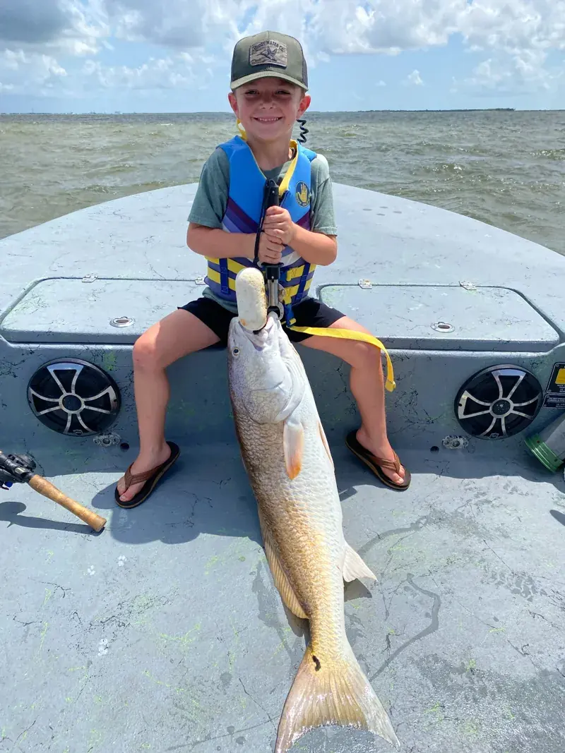 Young angler wearing a life jacket with a large redfish aboard the boat